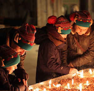 Image shows a family lighting a candle at Lichfield Cathedral while wearing their winter woolies